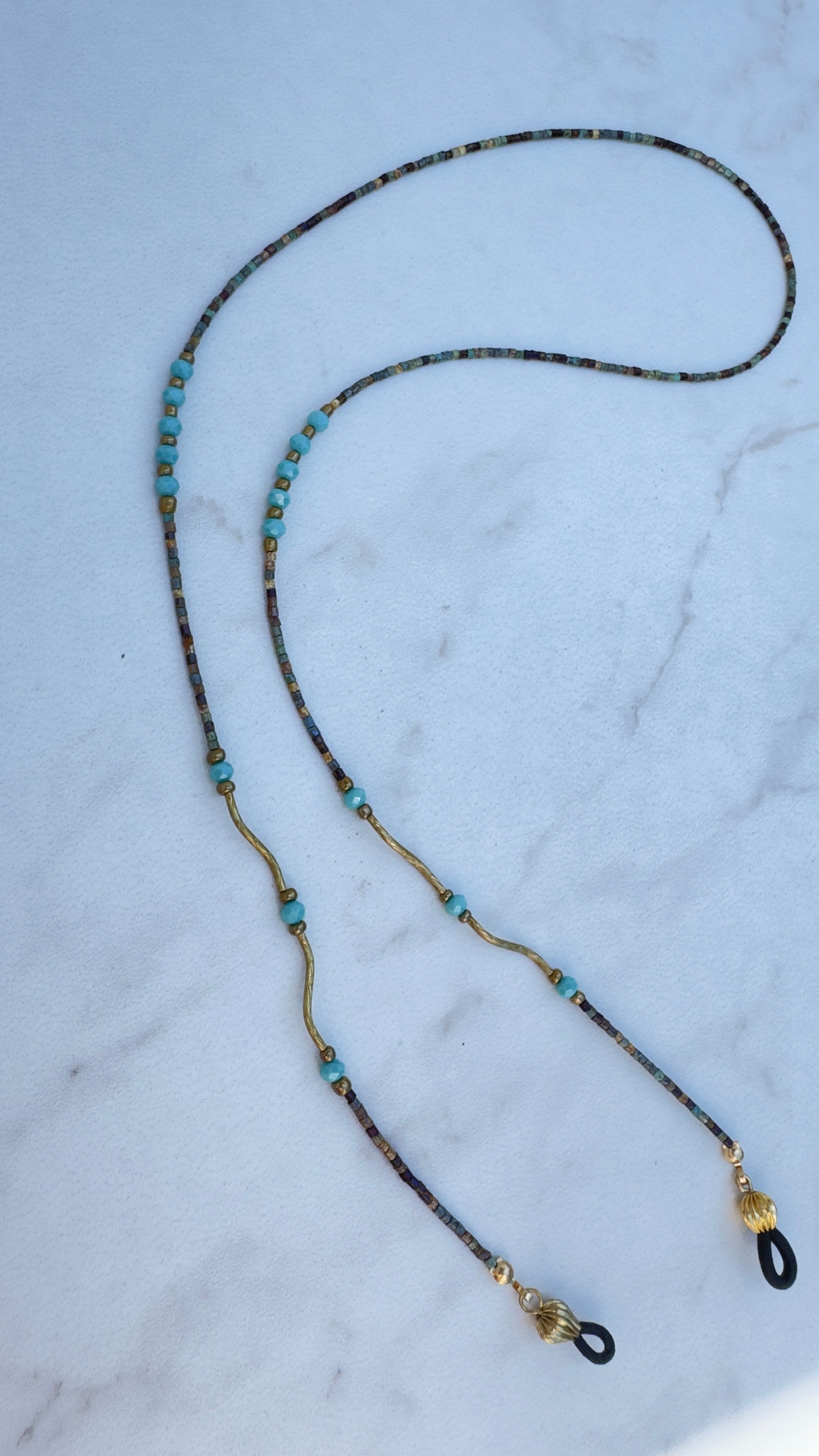 Beaded eyeglass chain with turquoise stones and gold accents on a marble surface
