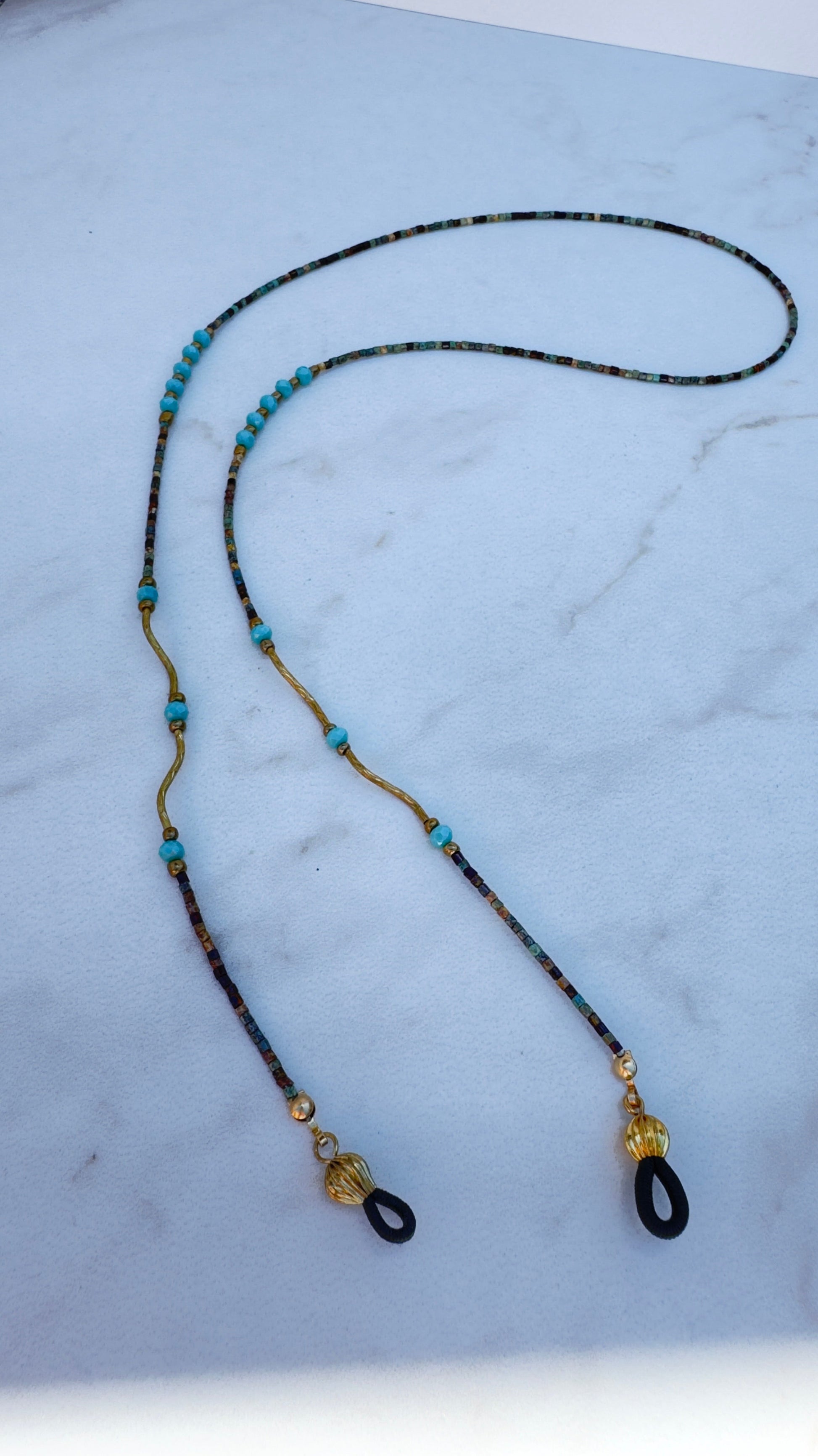 Beaded sunglasses chain with brown, gold, and turquoise beads on a light blue background